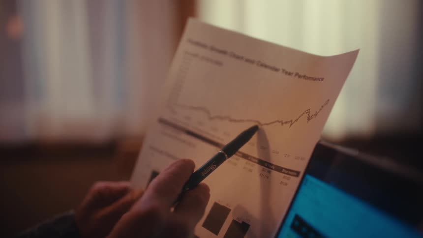 An elderly man intently reviews a financial portfolio growth chart tracking the data with a pen