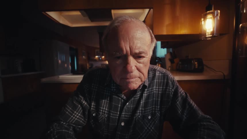 Elderly man sitting at his kitchen table with a calculator and documents opens his laptop