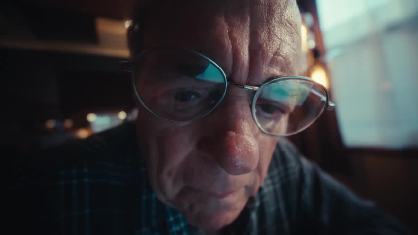 Elderly man with glasses sitting down typing on a calculator