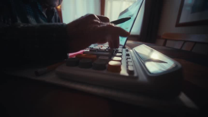 Elderly man using a laptop and calculator on a wooden table to review financial data