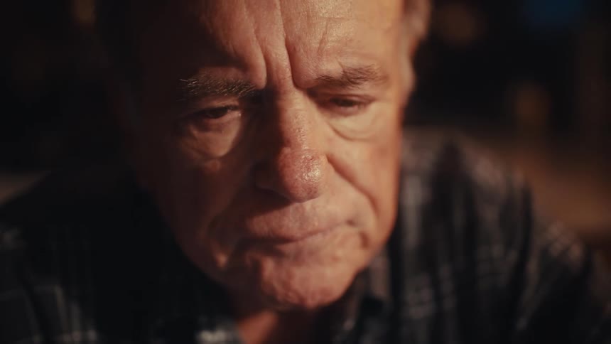 An elderly man in a plaid shirt is shown working at a desk alternating between using a calculator and typing on a laptop the video captures his focused expressions in closeup shots as he adjusts his glasses and looks thoughtfully toward his screen