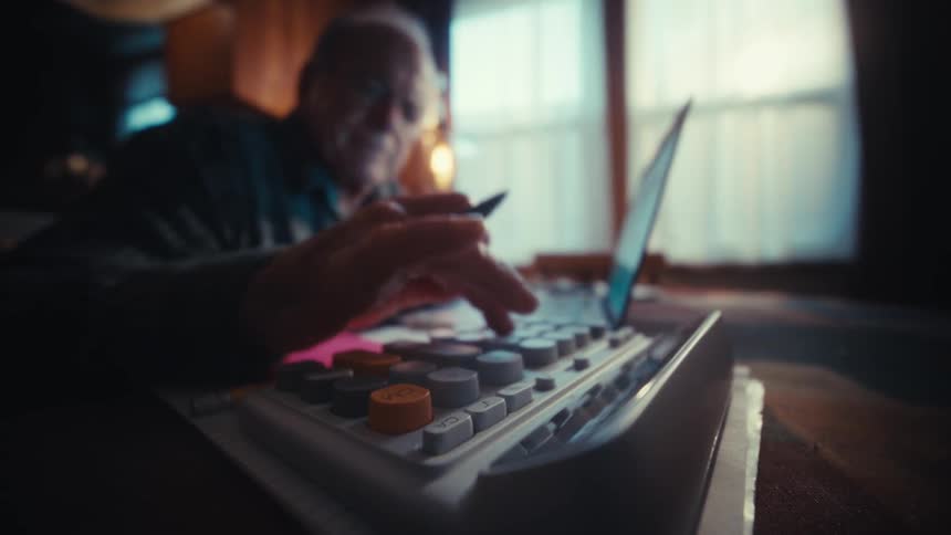 Elderly man sitting typing on a calculator