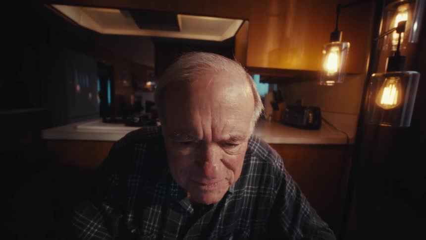 Elderly man sits intently in front of a laptop