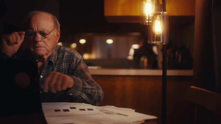Elderly man working on his finances at home in the evening stops to think