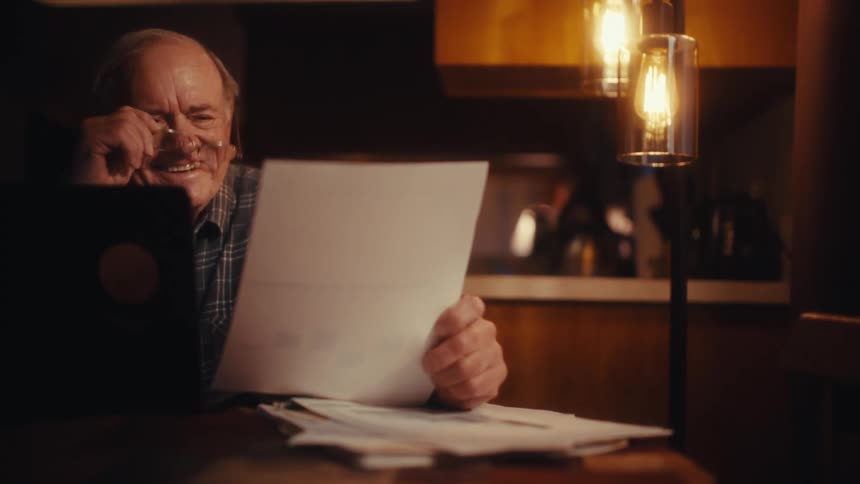 Elderly man sits in front of a laptop reading a document and looking happy