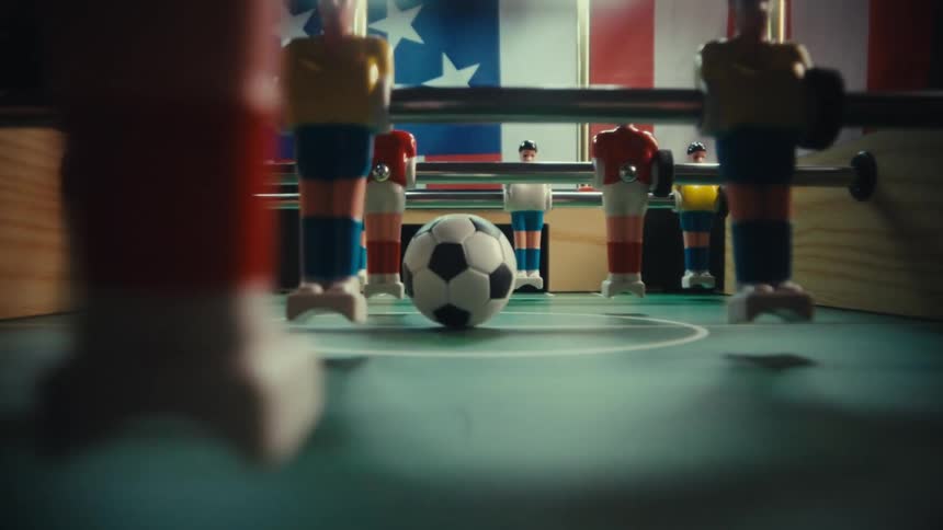 Soccer ball positioned at the center of a foosball table between aligned player figures