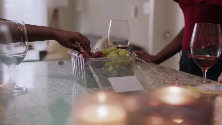 Women eat grapes and drink wine around a kitchen counter