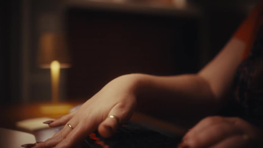 Hands type on a mechanical keyboard at a dimly lit desk before pausing