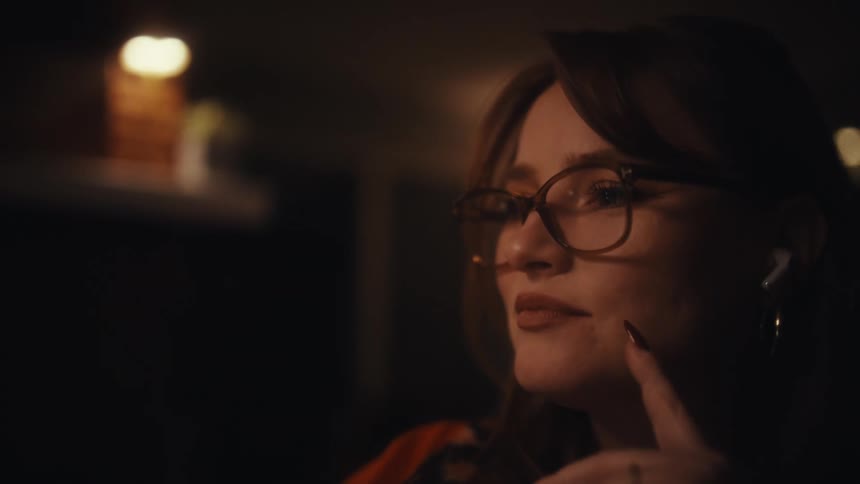A young woman sitting in an office wearing glasses and quietly contemplating