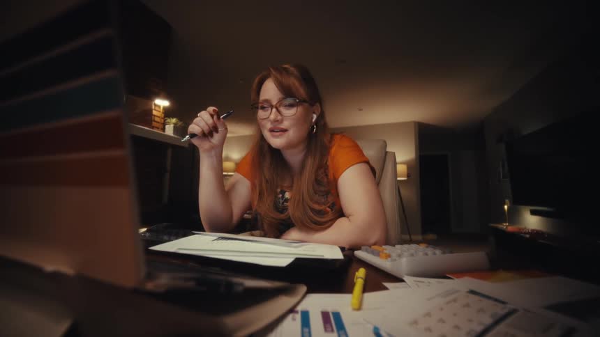 A woman engages in an office video call in a dimly lit home workspace