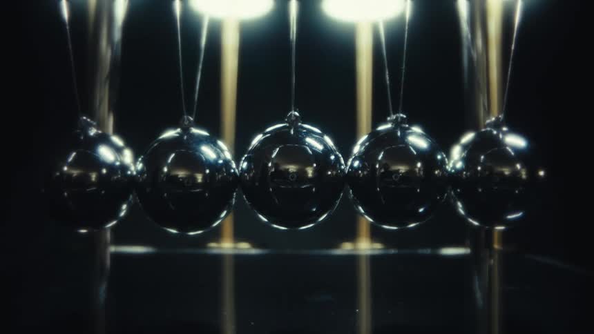 Five polished metal spheres suspended in a row creating a steady horizontal axis that remains centered as the camera zooms in