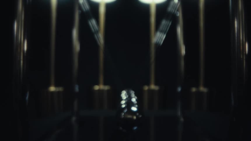 A newtons cradle with metallic spheres swings rhythmically in a dimly lit setting with three glowing lights in the background the camera remains focused on the central motion of the swinging balls against a dark reflective surface