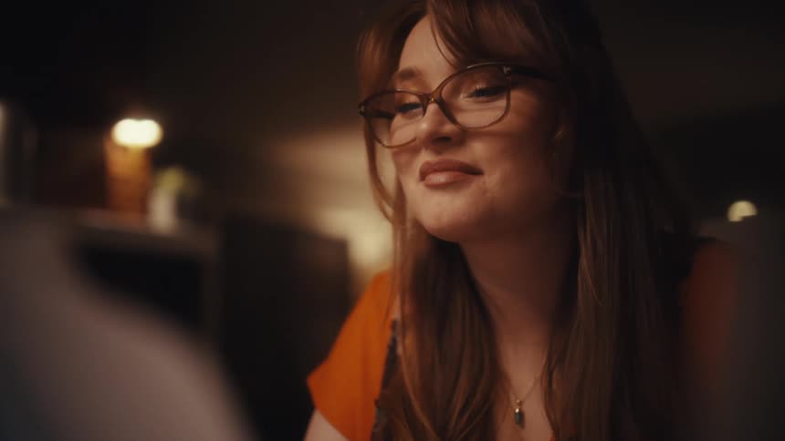 Closeup of a smiling woman with red hair and glasses reviewing printed financial documents and charts in a dimly lit office environment
