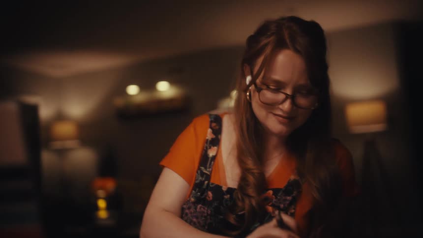 A determined woman smiles with satisfaction while working on her laptop in a dimly lit office