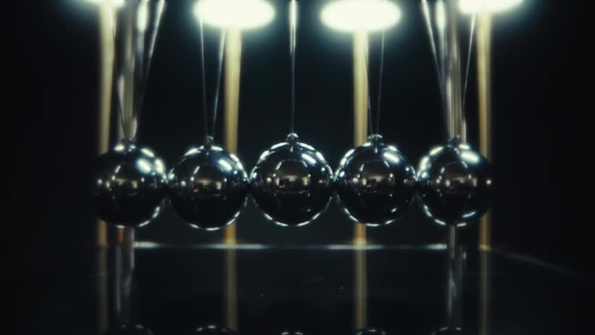 Aligned metal spheres in a pendulum device with reflected overhead lighting