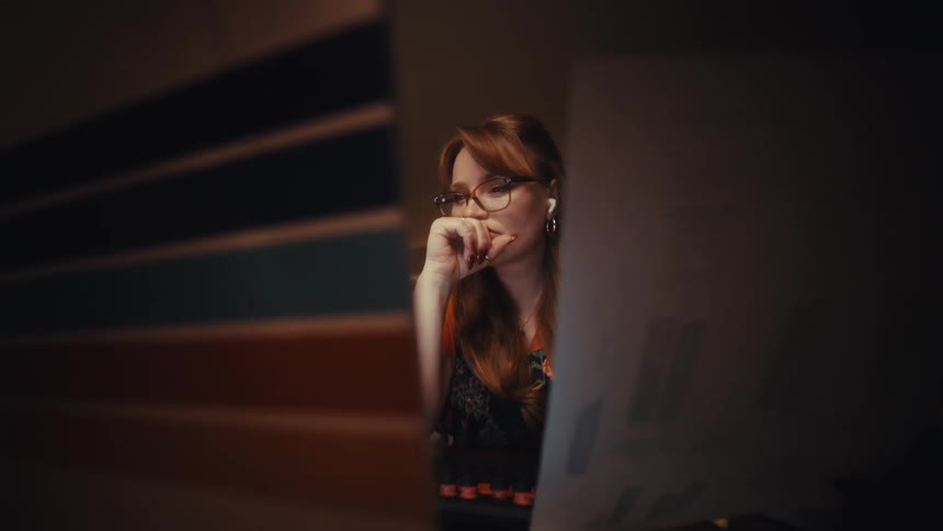 A woman focuses intently on her laptop while working at her desk in a dark quiet room