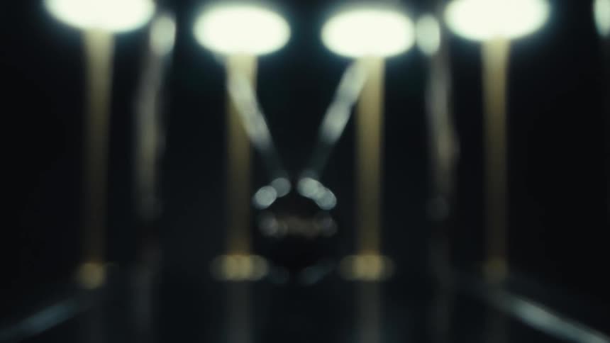 Balls in a newtons cradle swing back and forth as lights above glow