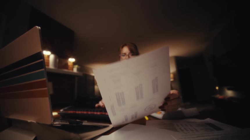 Woman typing on a laptop and holding a sheet with graphical data