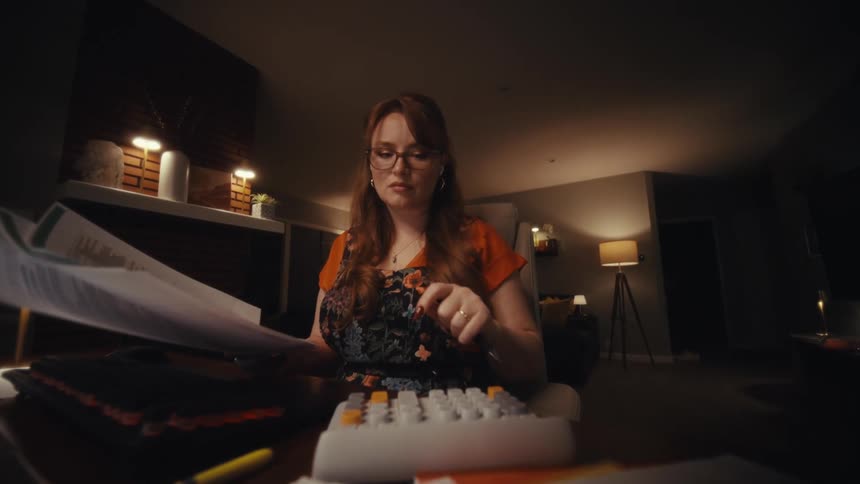 Woman is sitting typing on a calculator and holding documents