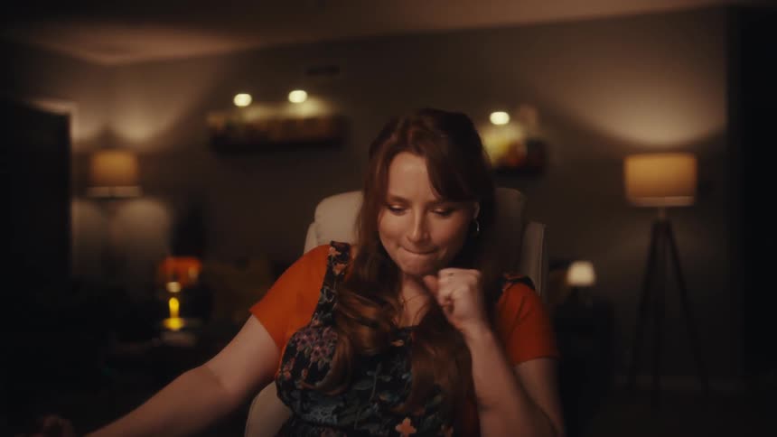 Young adult woman sitting down and reading on a laptop computer then smiling and cheering indoors during night time