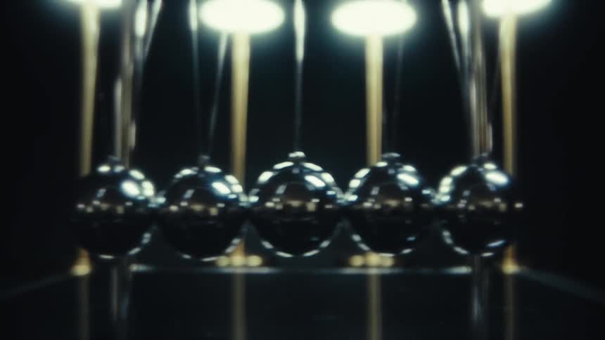 Closeup of a newtons cradle with polished metal balls in motion in a dark studio