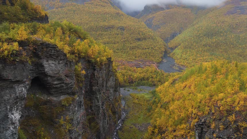 Aerial view of a misty mountain valley with autumn trees and a winding river