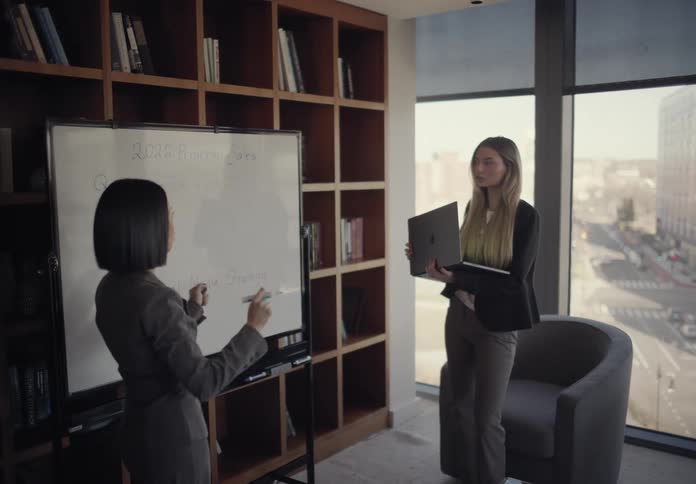 One woman speaks to another woman who is holding a laptop
