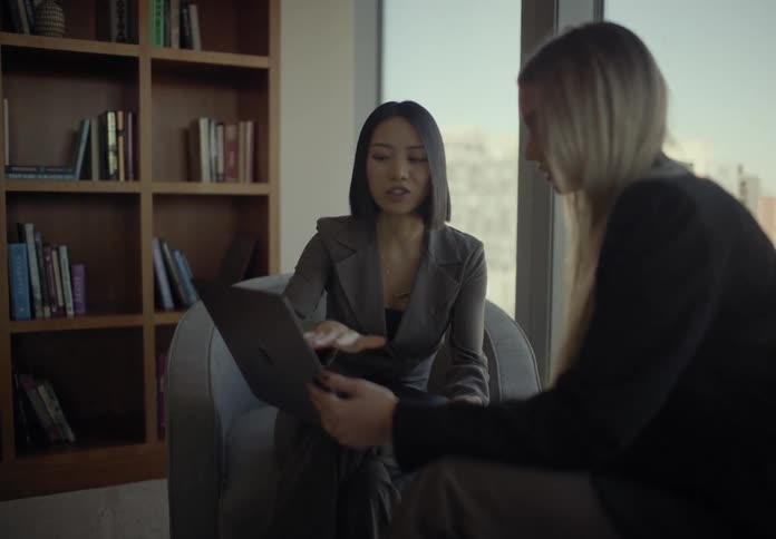 Two employees are collaborating on work over a laptop in a modern office lounge