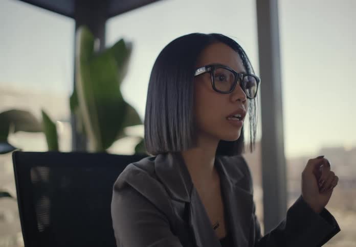 Woman sitting in an office setting holding a pen and talking