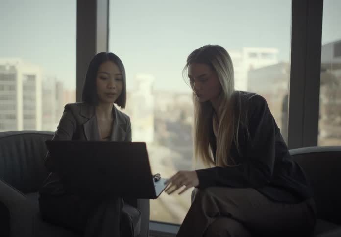 Two women sitting in an office looking at a laptop computer and talking
