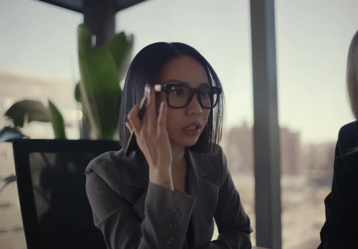 Woman sitting at a table in an office meeting holds her pen and moves her hand as she speaks