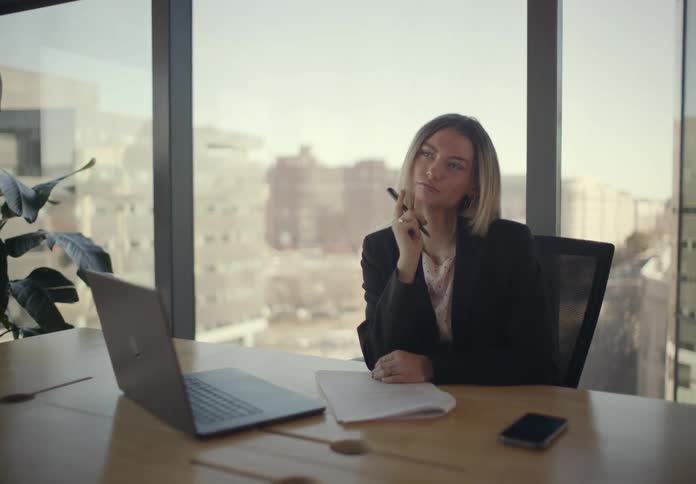 Thoughtful woman writing with a pen in an office room