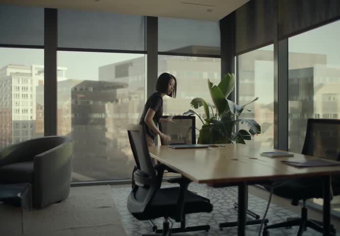 Woman walks into an office and puts her phone and laptop computer on the table as she sits down