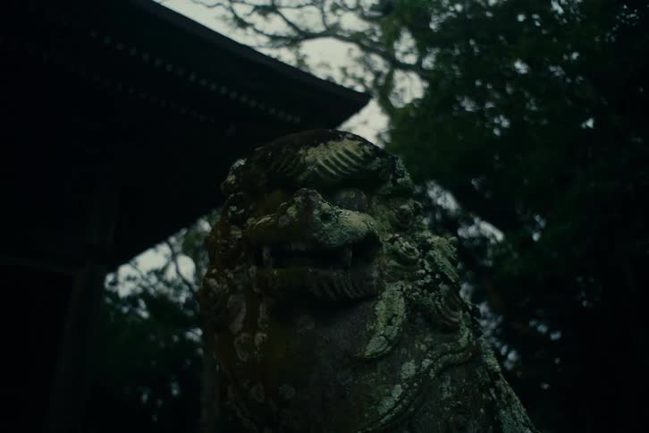 Stone guardian statue covered with moss positioned beside a traditional structure with surrounding trees