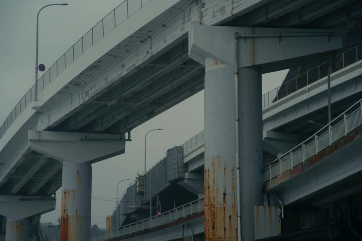 Large concrete highway overpasses stack on top of one another against an overcast sky the gray pillars show signs of weathering and rust as they support the multilevel traffic structures