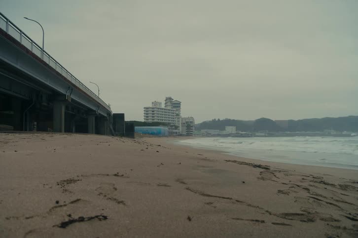 Wet sand on a beach next to an overpass with buildings in the background