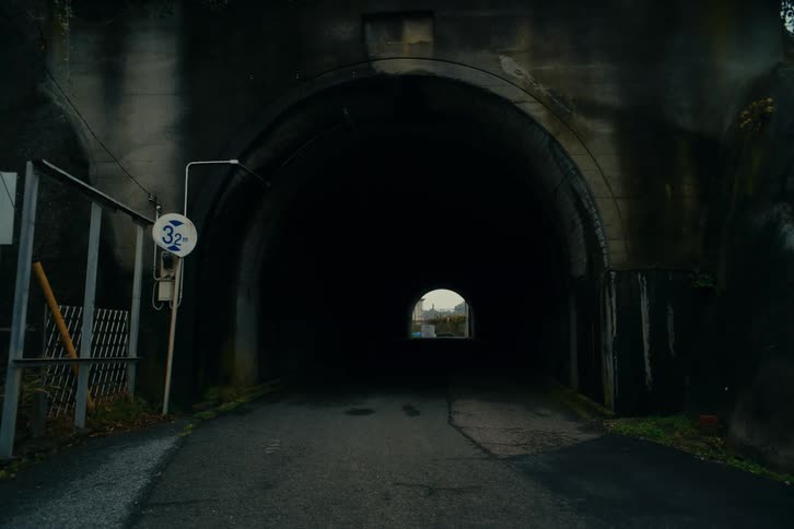 A dark road runs through a concrete tunnel toward a small opening of light at the far end