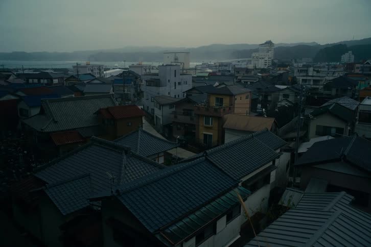 Cluster of residential rooftops in an urban area with buildings in the background and mountainous terrain under a cloudy sky