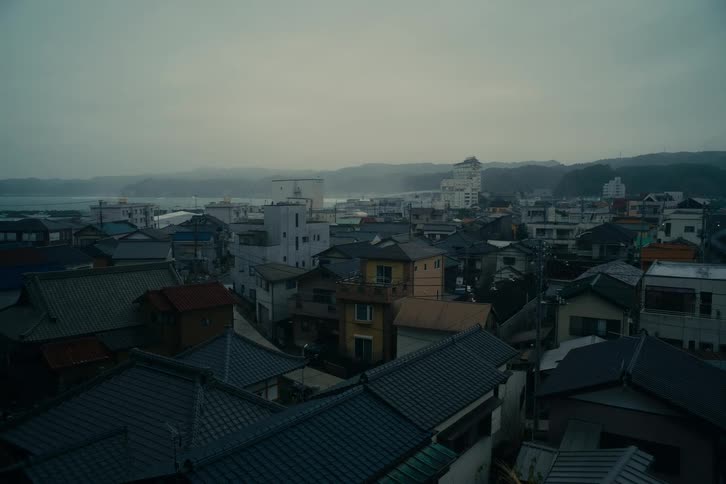 A dense cluster of coastal town buildings sits near the ocean under a gloomy overcast sky
