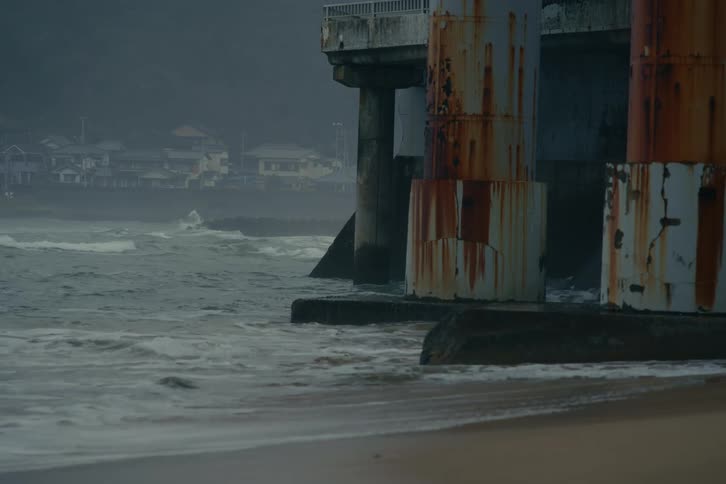 Waves crash along a beach and the supports of a large structure