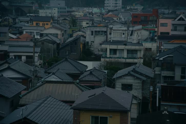 A highangle static shot overlooks a dense residential neighborhood showing a variety of multistory houses with tiled roofs and neutralcolored facades tightly packed together