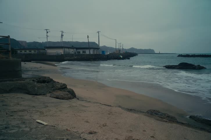 Utility poles and wires near buildings on the coast as waves roll in to shore and over the beach