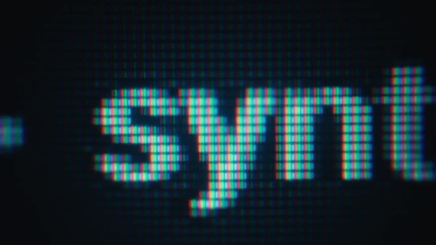 A macro closeup shows white digital text scrolling horizontally across a dark screen revealing pixels on the display grid