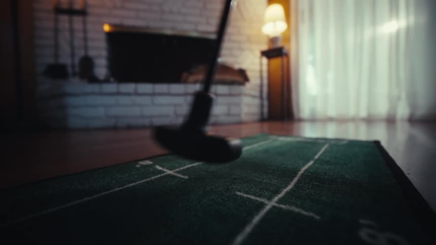 A putter strikes a baseball patterned golf ball on an indoor putting green