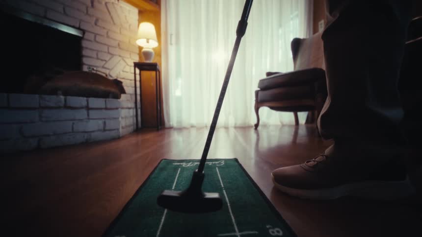 An adult putts a golf ball on an indoor putting mat in the living room