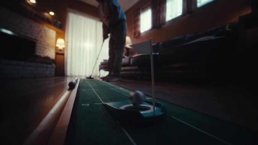 Man playing indoor golf putts the ball into the hole