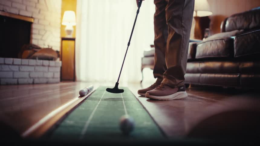 Man holds a golf club as he putts a ball in his living room