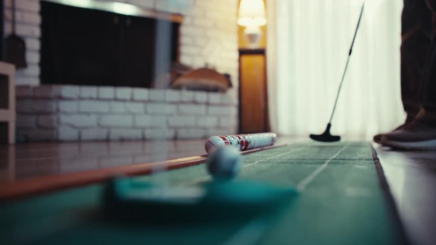 An adult putts a golf ball on an indoor putting mat in a living room