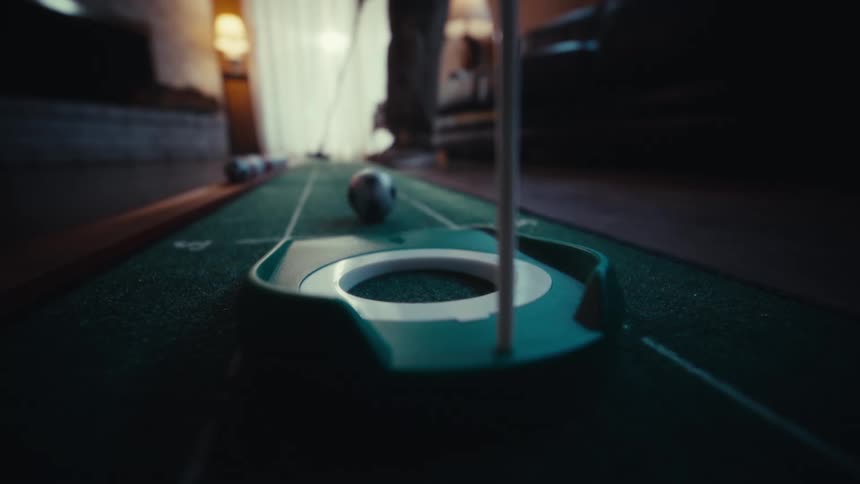 An adult putts a golf ball on an indoor putting mat in a living room