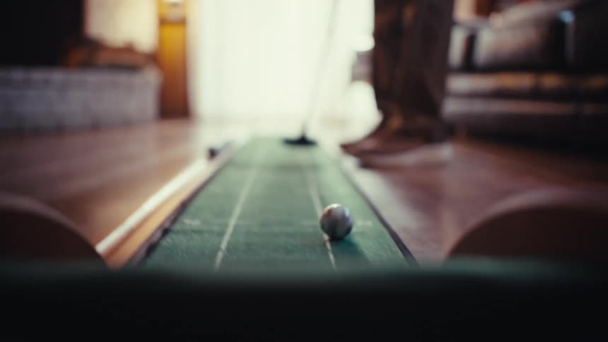 An adult playing golf in his living room hitting the ball with a club